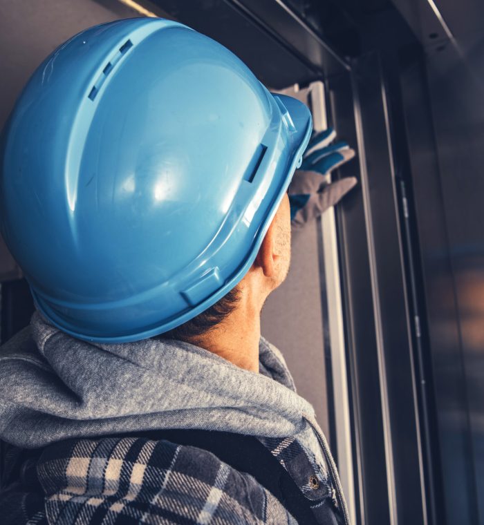 Elevator Technician Taking Close Look on the Finished Shaft Door Caucasian Elevator Technician Wearing Blue Hard Hat Taking Close Look on the Finished Shaft Doors.