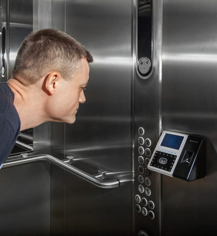 A man shows his face to a fingerprint access control terminal with a facial recognition function installed in the elevator of a business center.