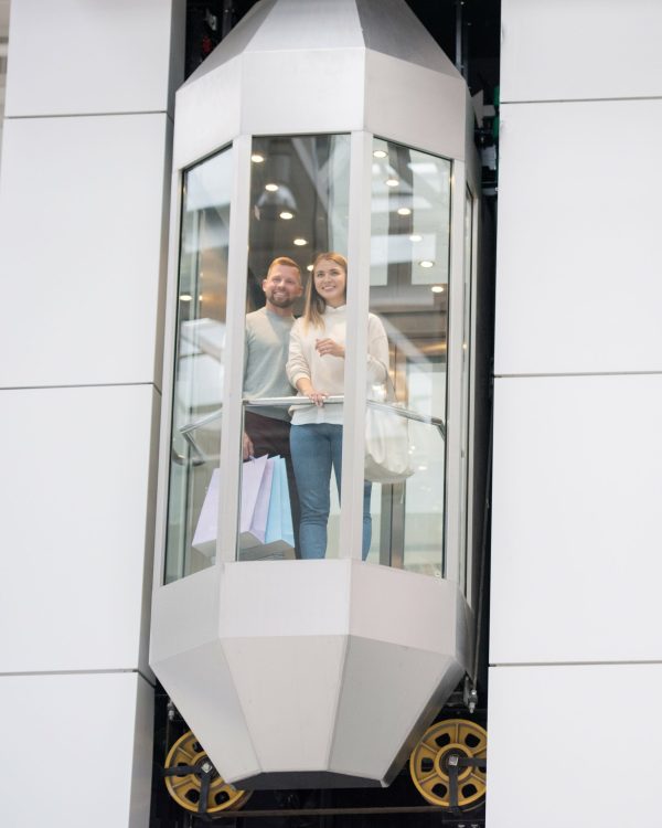 Young dates standing in one of elevators and looking through window while enjoying shopping in the mall on black friday